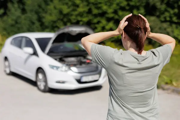 woman driver standing near a problem car and holding her head