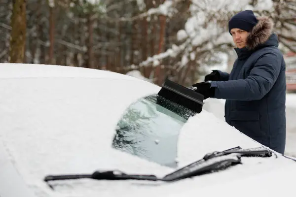 young man cleaning a snow covered car with brush after snowfall