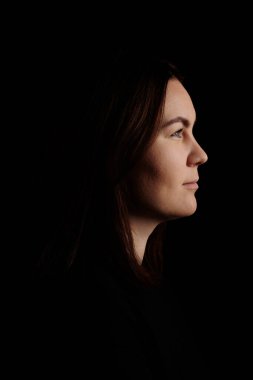 Koyu arkaplanda güzel bir genç kadının yan görünümü.