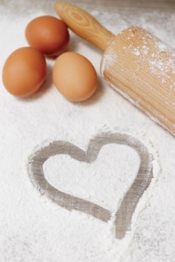 Yuvarlanan iğne, yumurta ve kalp şeklinde ahşap zemin üzerinde un.