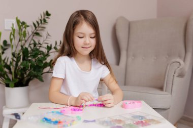 Odasında pembe ve mor boncuklu mücevherler yapan bir kız.