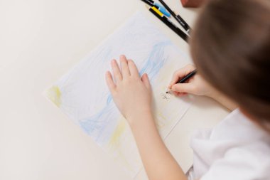 Kız ellerinin üst görünümü resmi kağıda çizer ve boyar