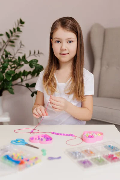 Girl making beaded jewelry at table in room
