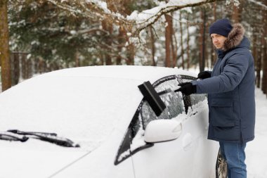 Genç adam arabasını fırçayla kardan temizliyor.
