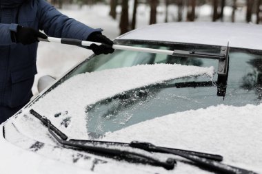 Erkek sürücünün kar yağdıktan sonra arabasının ön camını temizlemesine yakın durun.