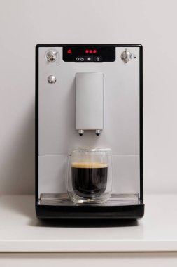 Modern kahve makinesi. Mutfaktaki masanın üzerinde cam bir fincan espresso.