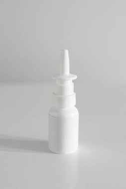 Burun spreyi etiketi olmayan beyaz bir şişe beyaz bir masada dikey duruyor.