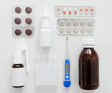 Dijital termometre, burun spreyi, haplar ve beyaz masadaki boğaza sprey.