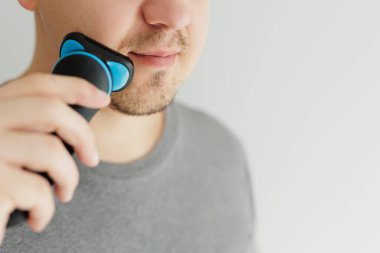 Genç adam siyah bir budama makinesiyle sakalını kesiyor.