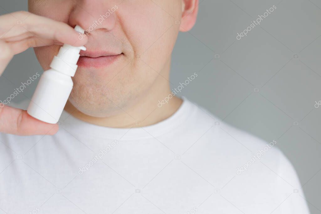 Closeup of young man spraying drops in nose in white tshirt with copyspace