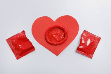Kırmızı kalbin üst görüntüsü ve beyaz üzerine açık prezervatif.