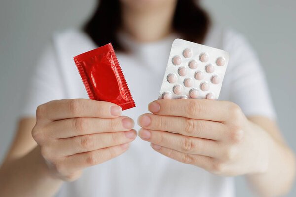 Woman in white tshirt showing pills and condom in hands