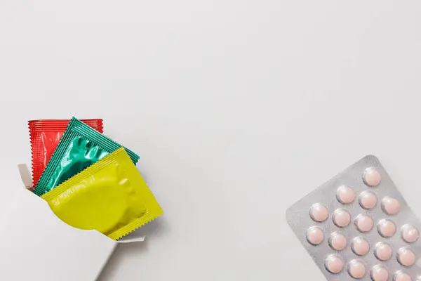 白色包装 黄色避孕套和带彩色的药丸 免版税图库图片