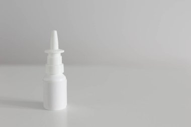 Burun spreyi etiketi olmayan beyaz bir şişe, telif uzayı olan beyaz bir masada dikey duruyor.