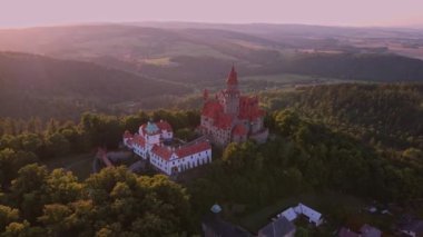 Batan güneşle aydınlatılan bir orman manzarasında romantik bir masal kalesinin havadan görünüşü. Ağaçlarla çevrili Gotik bir kale. Bouzov Şatosu, Çek Cumhuriyeti.