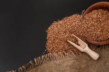 Tahta kaşıkta karabuğday tohumları ve siyah arka planda dağınık, seçici bir odak. Metin uzayı