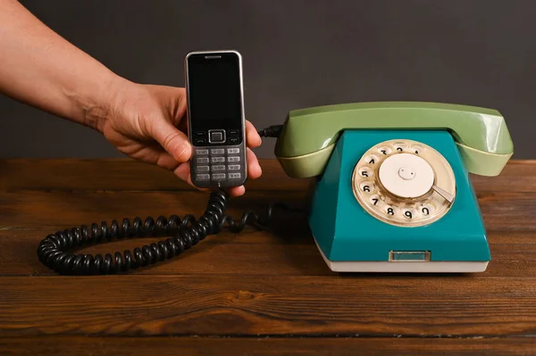 an old push-button mobile phone in a woman\'s hand next to an old vintage dial phone.