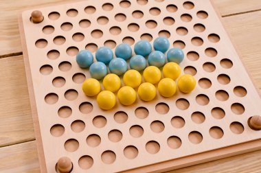 A board game made of wooden beads on a wooden background. Close-up. The balls are yellow and blue. Develop fine motor skills, logical thinking.