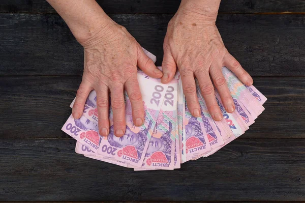 Masanın üzerinde yaşlı bir kadının ellerinde Ukrayna Hryvnia 'sı.