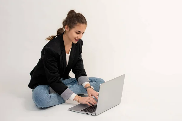 stock image the girl is sitting on the floor and working or communicating on a laptop.