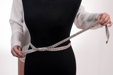 Bir terzi kız bir mankenin genişliğini ve uzunluğunu ölçer. Moda kıyafetleri terziliği. Beyaz arkaplanda yakın plan.