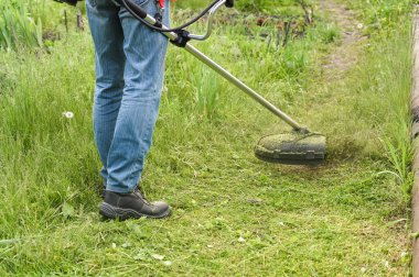 Şehir parkında ya da arka bahçede elektrikli çim biçme makinesiyle çim biçen bir işçi. Çim biçme makinesiyle çim biçme işlemi
