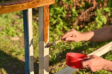 Bir insan boyayla ahşap boyar. Parlak güneşli bir günde bahçede