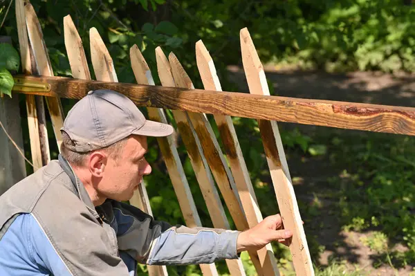 A male carpenter makes a fence outdoors