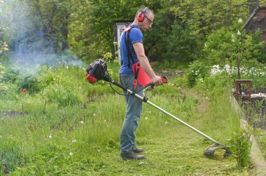 Çiftlik işçisi çimleri benzin tırpanıyla biçiyor.. 