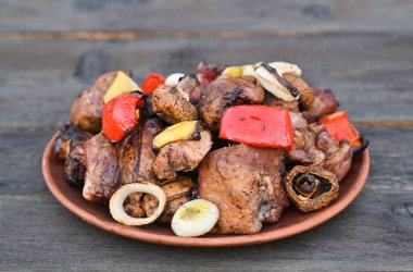 Izgarada yapılan et ve sebzeler ahşap bir masada bir tabakta yatıyor..