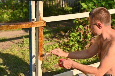 Açık havada vernikle ya da ahşap lekeyle resim yapan biri.