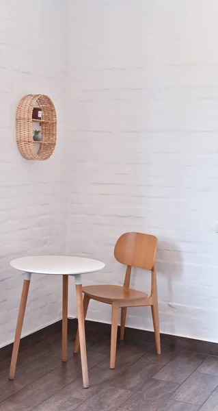 A table and a chair in the corner of the room. against the background of a brick white wall.