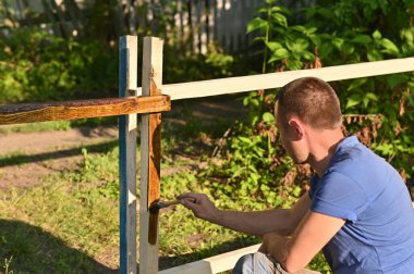 Açık havada elinde fırçayla ahşabı cila ya da lekeyle boyayan biri..