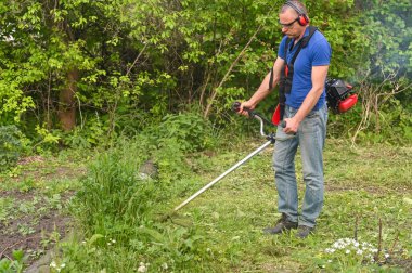 Elinde budama makinesi olan bir adam çimleri biçer..