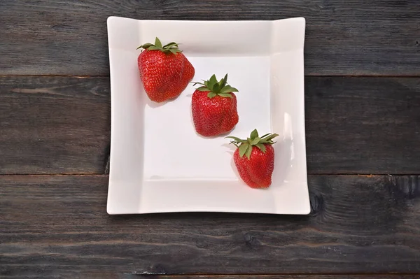 Drei Erdbeeren Auf Einem Weißen Teller Auf Einem Hölzernen Hintergrund — Stockfoto