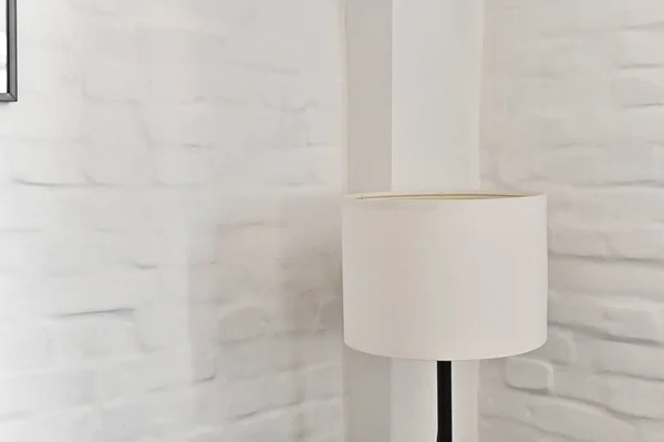 a white floor lamp in the corner of the room against a white brick wall.
