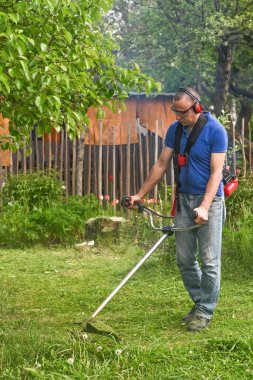 Bir çiftçi çim biçme makinesiyle uzun yeşil çimenleri biçer..