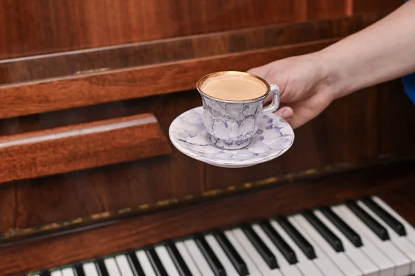 the concept of a musical pause during music lessons. A cup of coffee in his hand against the background of an old piano.