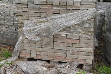 Caddedeki bir inşaat deposunda paletlere tuğla yerleştiriyorlar. Onarım kavramı