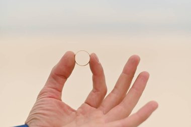 Yakından altın bir yüzük. Gelinin alyansı adamın elindedir.