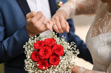 Kırmızı güllü gelin ve damat. El ele tutuşarak.