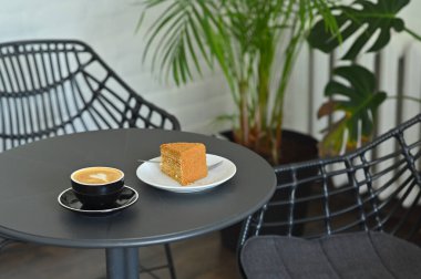 Bir fincan sıcak kahve, içinde kalp deseni ve çay tabağının üstünde kek var.