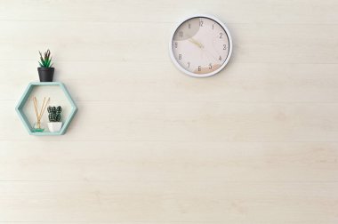 Odanın iç duvarında bir kopyasal alan var. Duvarda bir saat, saksıda çiçekler ve bir koku yayıcı var.