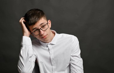 Şüpheci bir çocuk, düşünüyor, başını kaşıyor. Gri bir arkaplanda.