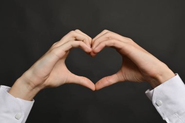 Aşk jesti, eller gri arka planda kalbi gösterir. Bu jest romantizmin sembolü, yakın plan.