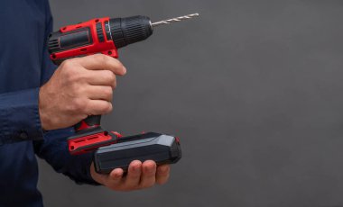 Adamın biri tornavidaya pil takıyor. Gri bir arka plana yakın plan. Boşluğu kopyala