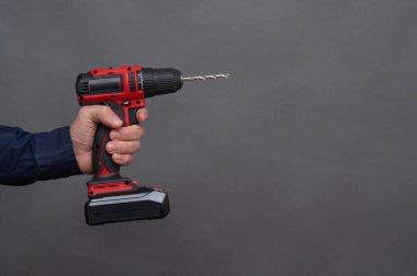Gri arka planda, bir adamın elinde elektrikli tornavida.. 