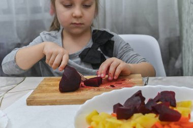Küçük bir kız salata hazırlar, sebzeleri tabağa koyar.