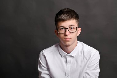 Gözlüklü ve gri arka planda beyaz gömlekli sevimli bir gencin portresi. Boşluğu kopyala