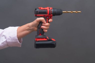 Gri arka planda matkapla bir kadının elinde elektrikli tornavida.